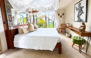 Quarto com uma cama grande, uma mesa, uma cadeira e varanda com vista.