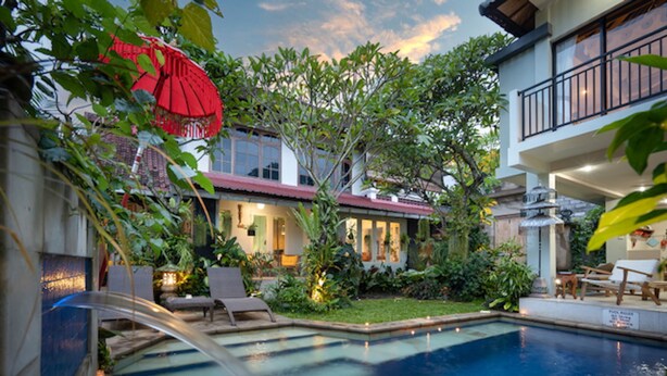 A swimming pool with a waterfall feature, surrounded by lush greenery and a well-lit patio area. - Angel House Ubud Eco Villa (Mas)