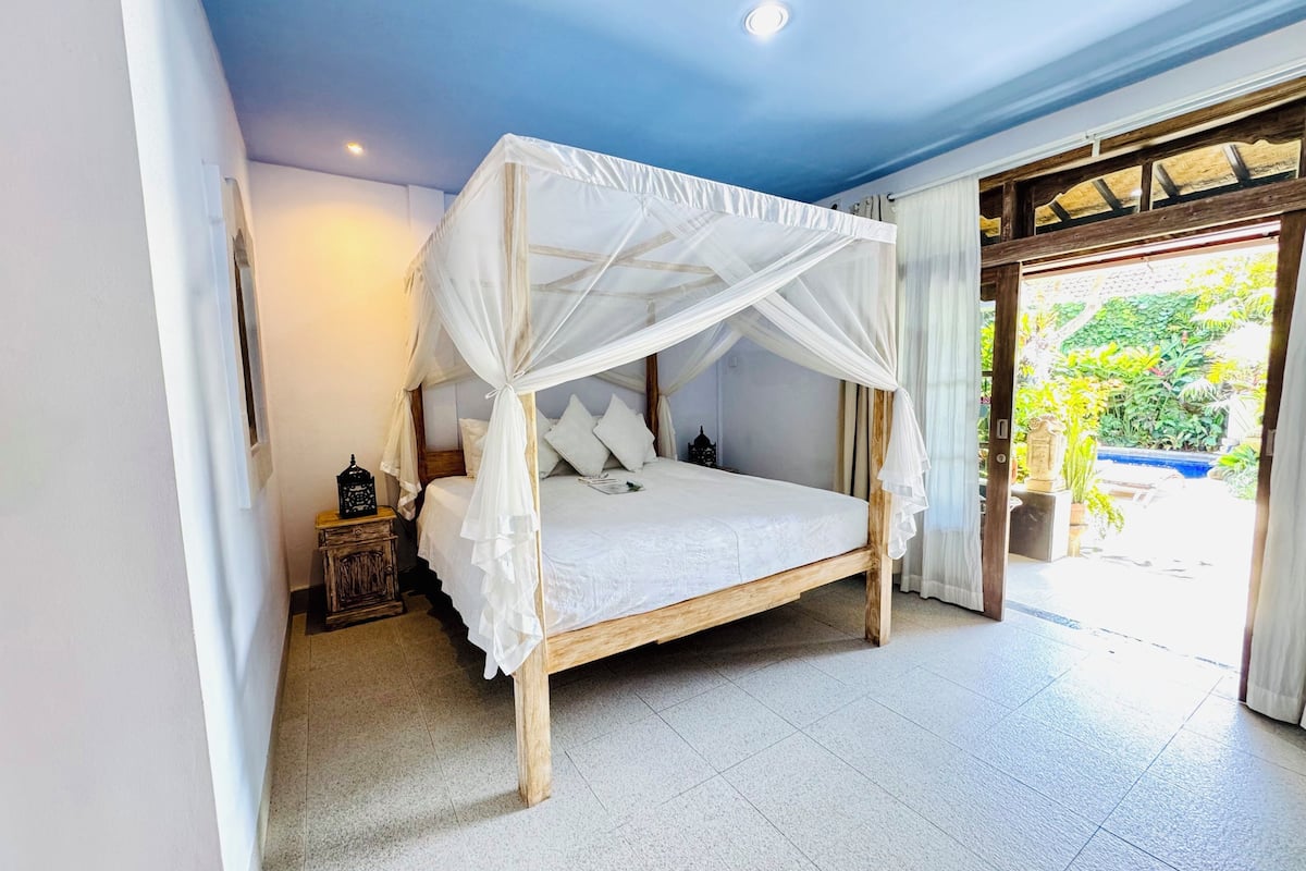 A bedroom with a canopy bed, a nightstand, and a view of a garden.