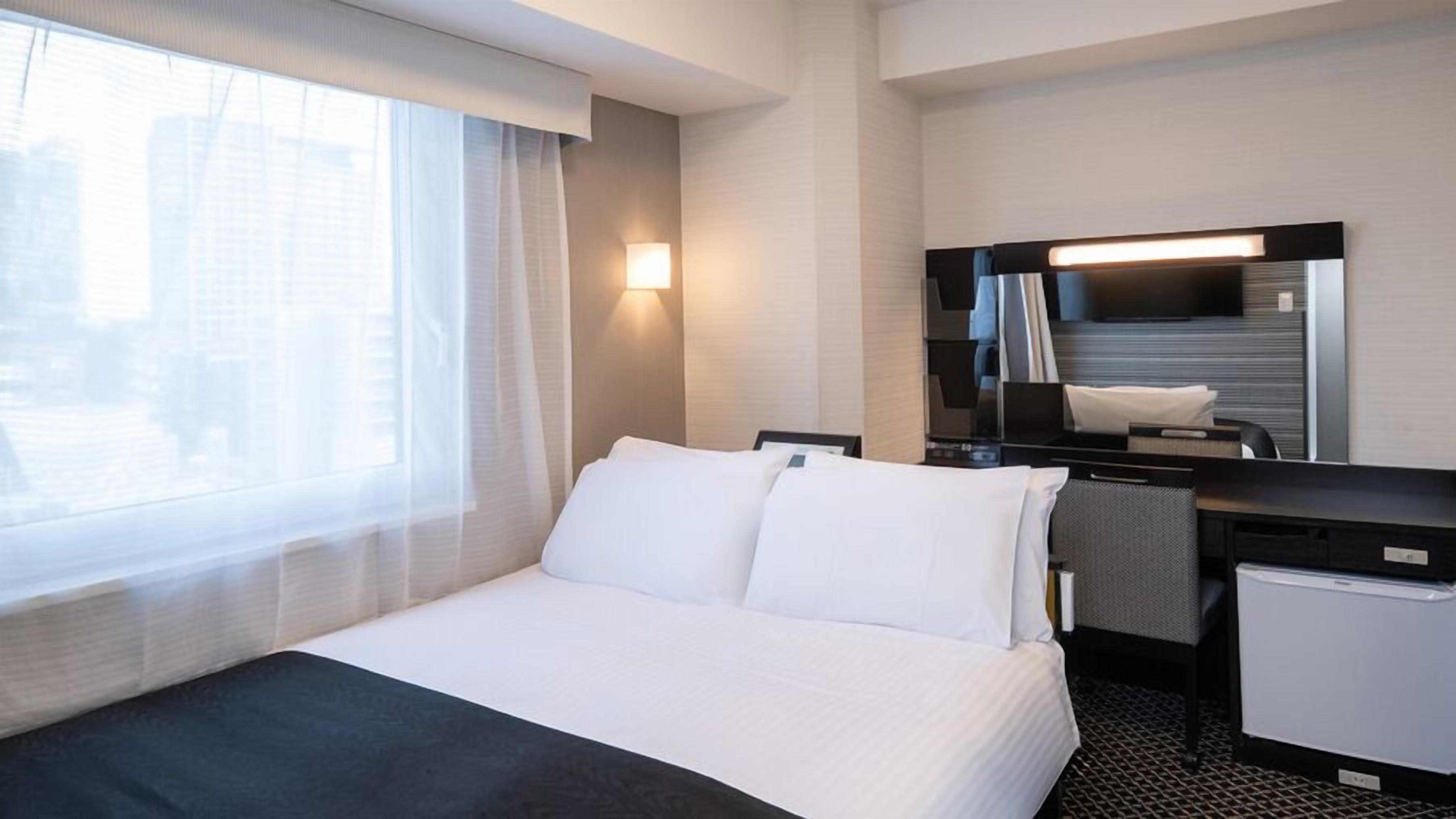 Quarto de hotel com cama, escrivaninha, espelho e janela com cortinas.