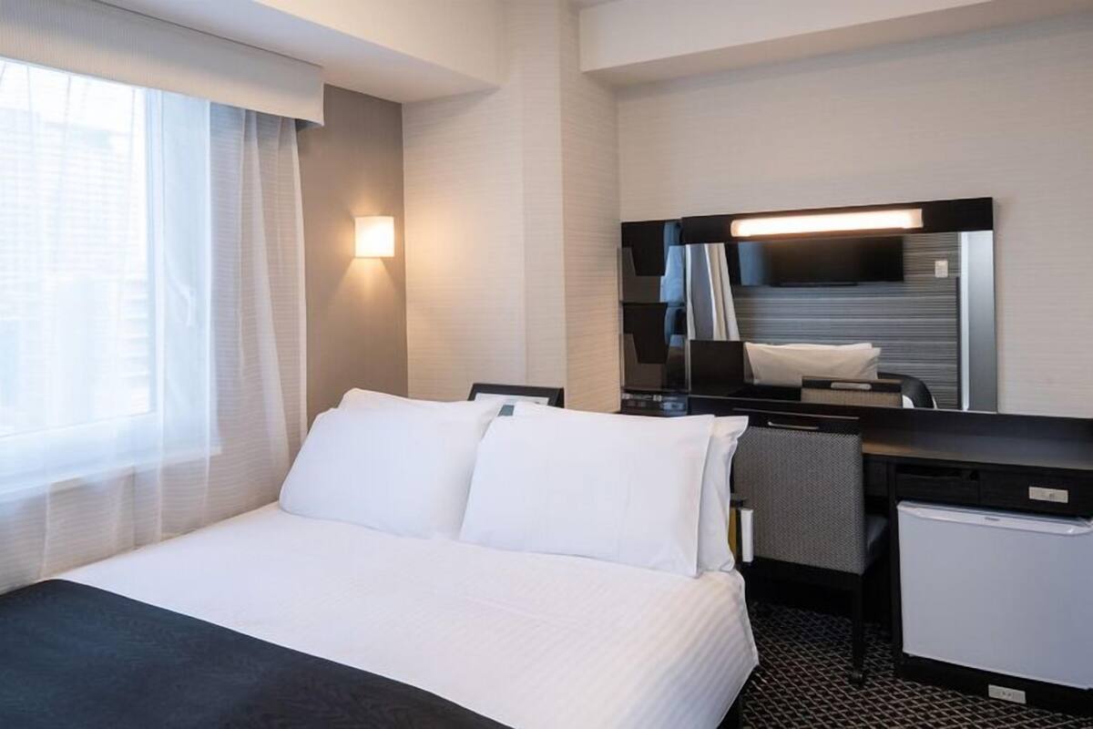 Habitación de hotel con cama, escritorio, espejo y ventana con cortinas.