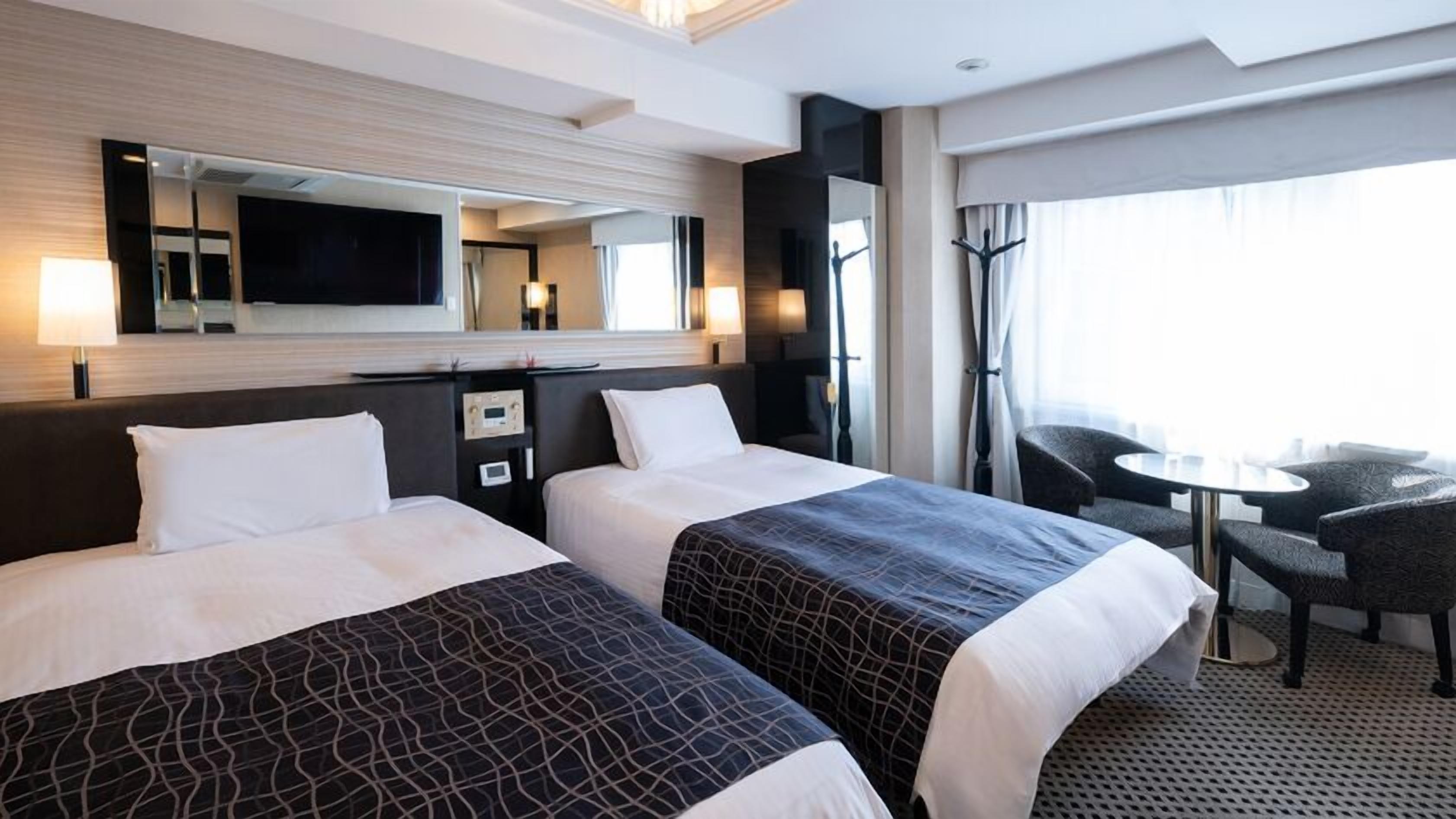 Quarto de hotel com duas camas, televisão, escrivaninha e uma cadeira.