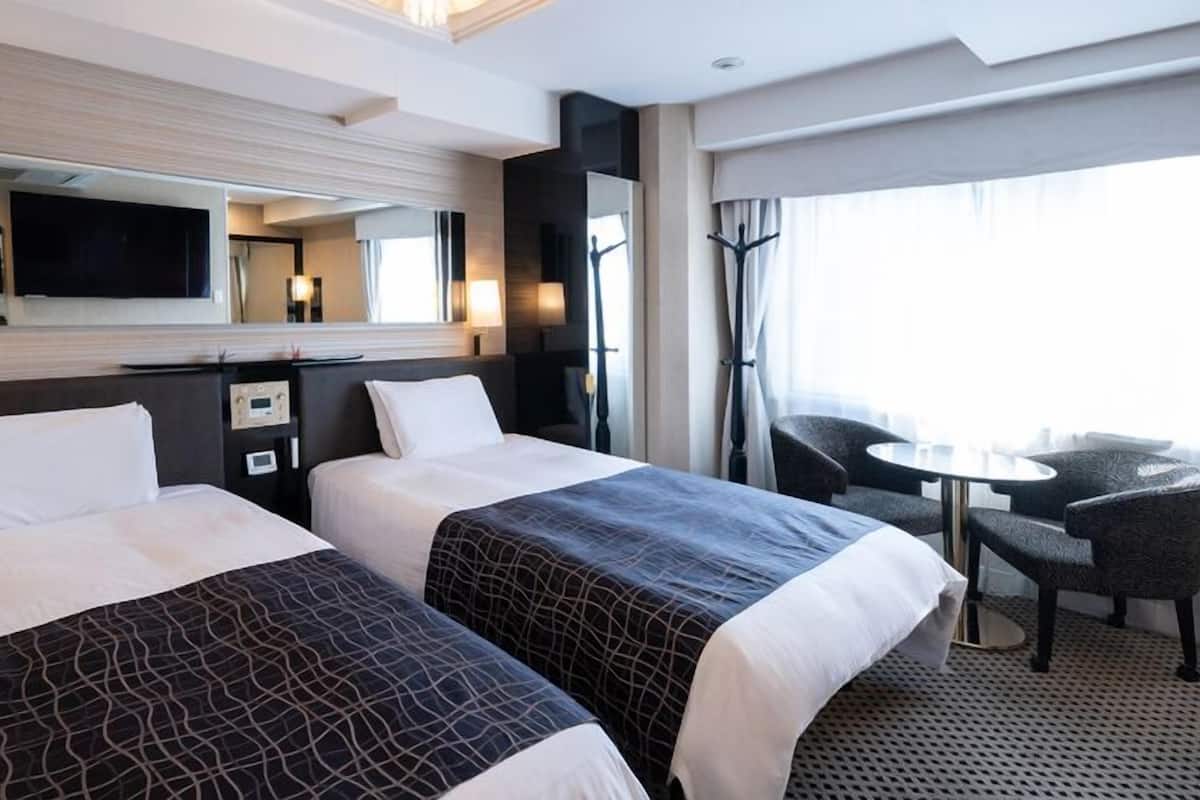 Habitación de hotel con dos camas, televisión, escritorio y una silla.