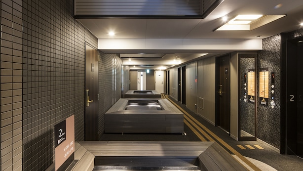 A modern hotel corridor with a central walkway, multiple doors, and a tiled wall. - APA Hotel Higashi Shinjuku Kabukicho Higashi (Tokyo)
