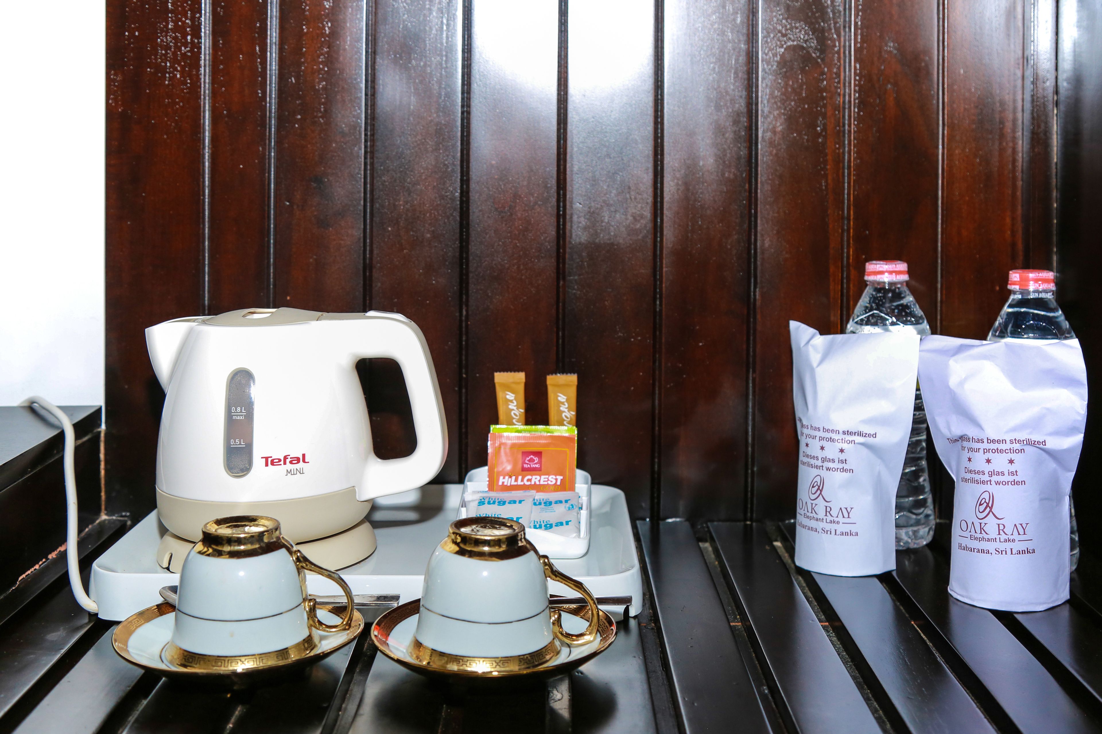 A minibar setup with a Teefal Mini kettle, Hillcrest sugar packets, and two bottles of water from Oak Ray.