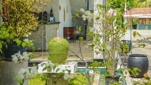 Un jardín con un gran macetero cubierto de musgo, una mesa de vidrio y diversas plantas en macetas.