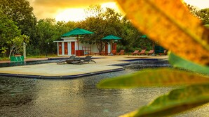 Un área de piscina con sillones y sombrillas, rodeada de vegetación.