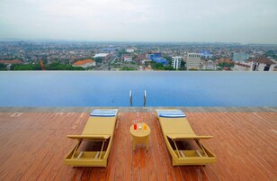 En infinitypool med solstolar och ett bord, med utsikt över stadens skyline.