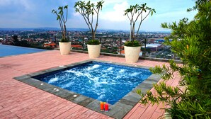 A rooftop pool with a view of a cityscape, surrounded by potted plants and a wooden deck. - Louis Kienne Hotel Pandanaran (Semarang)