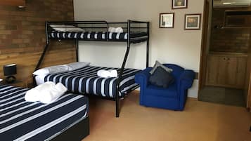 A room with two bunk beds, a blue armchair, a small table with a lamp, and a brick wall.