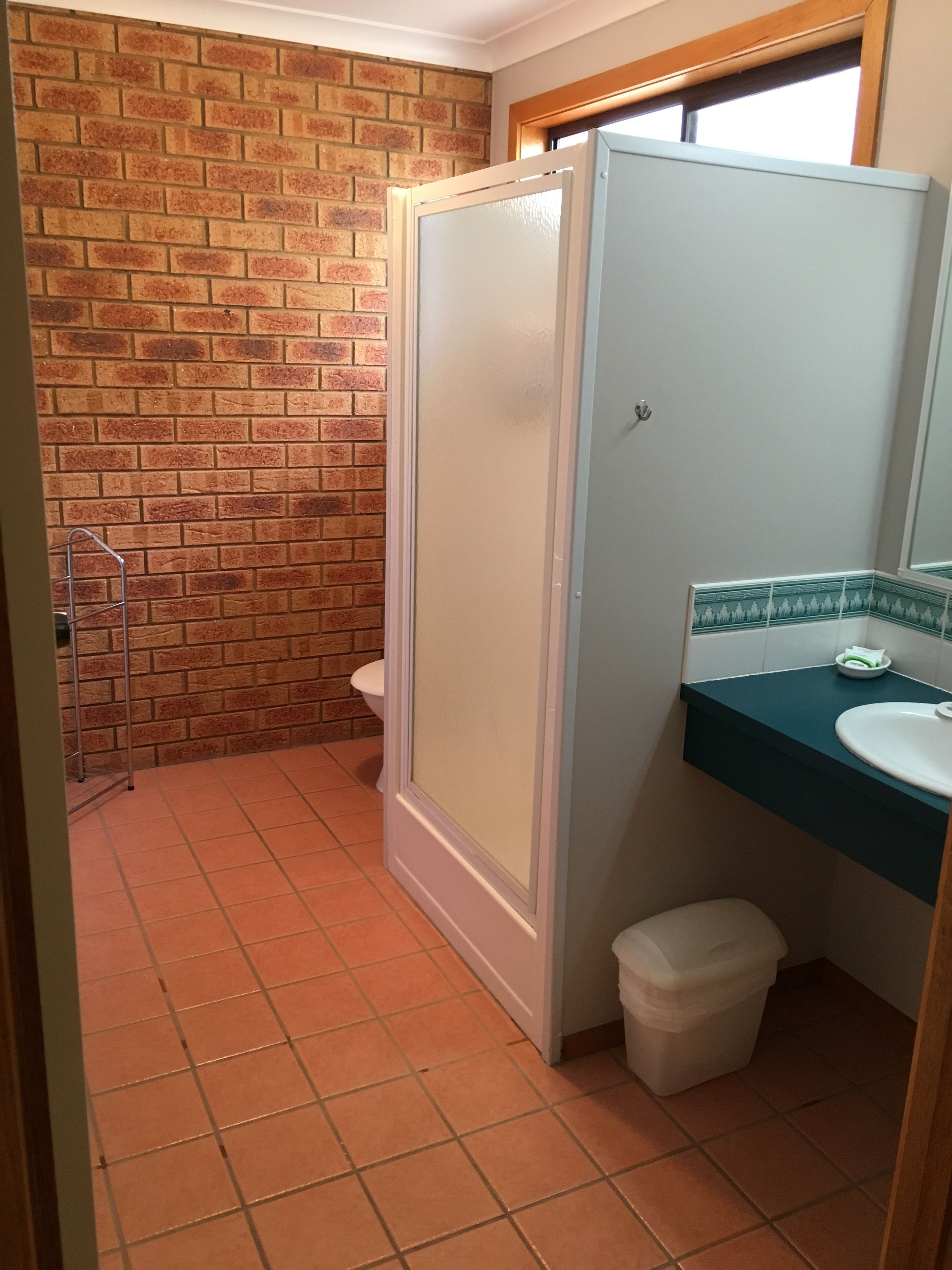 A bathroom with a tiled floor, a toilet, a shower enclosure, and a sink with a mirror.