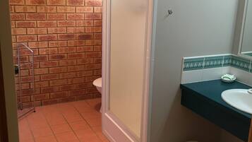 A bathroom with a tiled floor, a toilet, a shower enclosure, and a sink with a mirror.