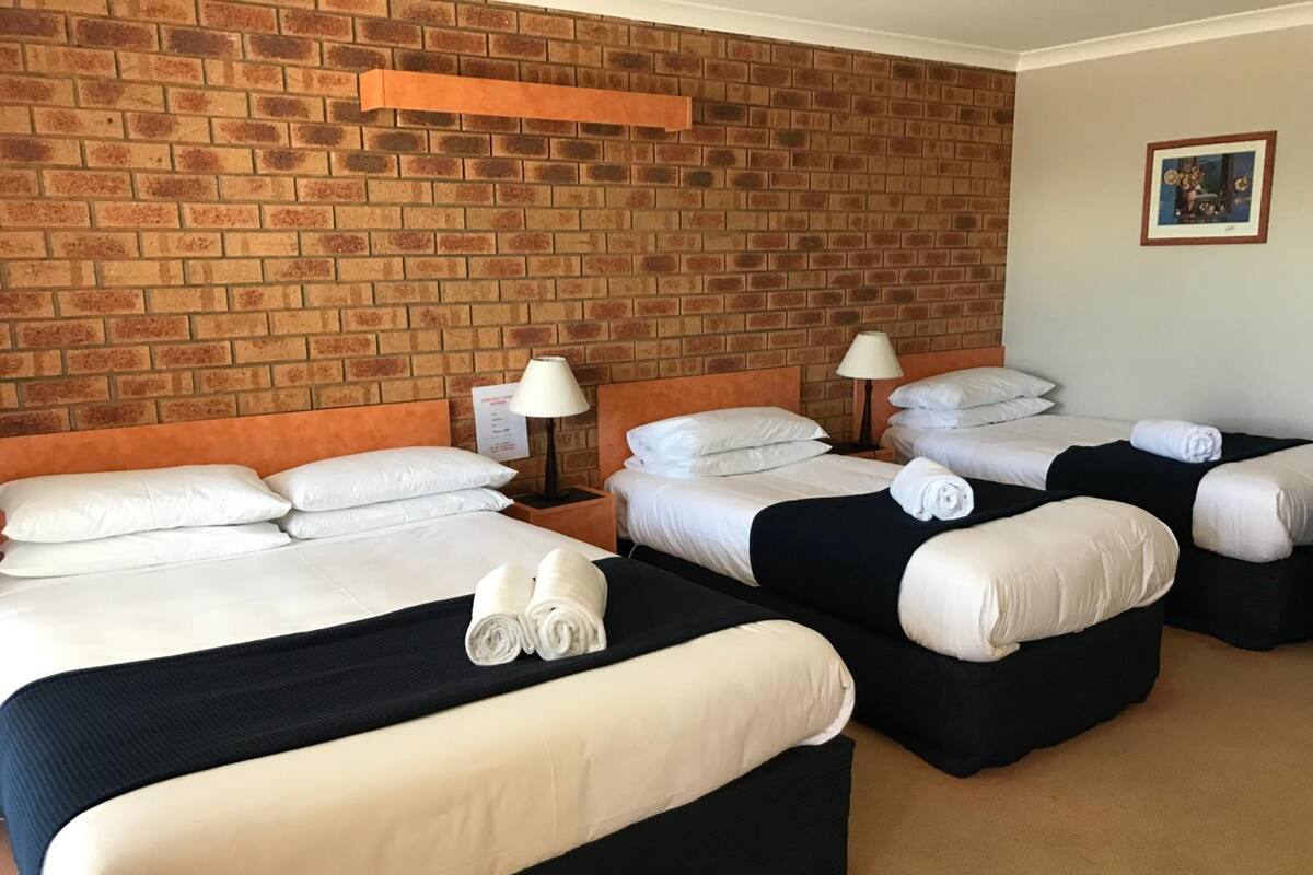 Habitación de hotel con cuatro camas, cada una con sábanas blancas y cabeceros negros. Hay dos lámparas de noche de madera.