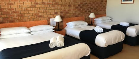 Ett hotellrum med fyra sängar, alla med vita sängkläder och svarta sänggavlar. Det finns två sänglampor på träbord som står vid sängarna.