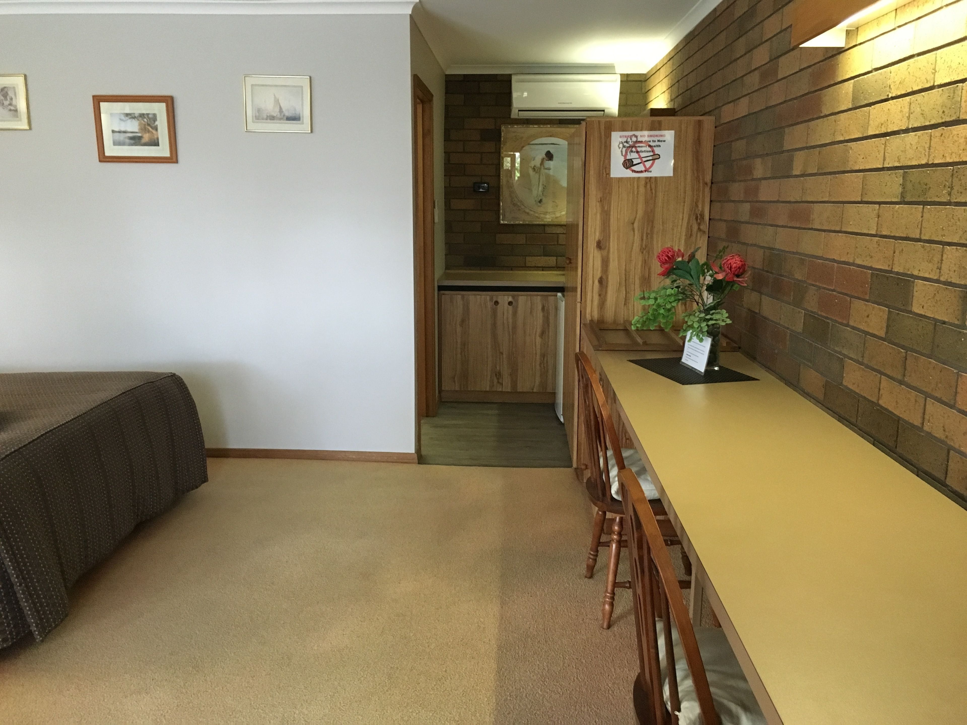 A hotel room with a bed, a wooden table with chairs, a brick wall, and a kitchenette in the background.
