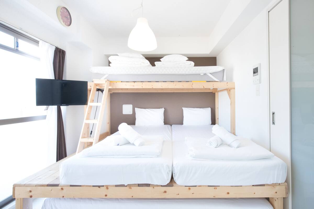A bunk bed room with two beds, a TV, a ladder, and a window.