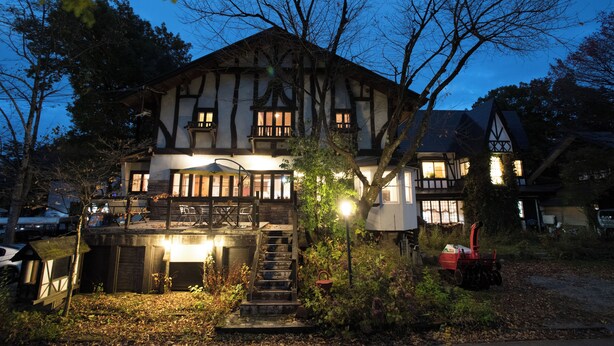 A traditional timber-framed house with a staircase leading to a deck, surrounded by trees and a garden. - Pension EastMountain Hakuba (Hakuba)