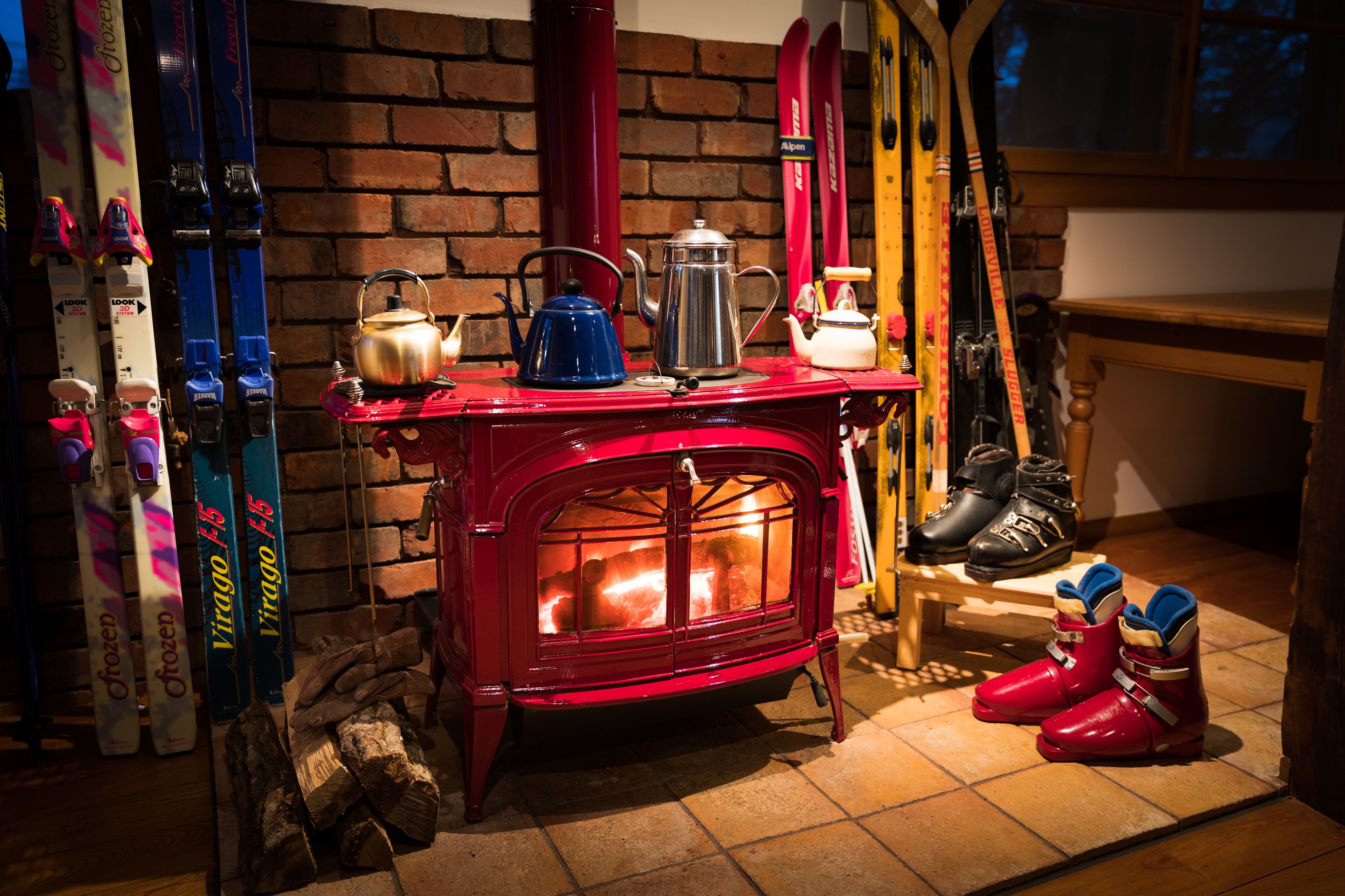 A red stove with skis and boots nearby.