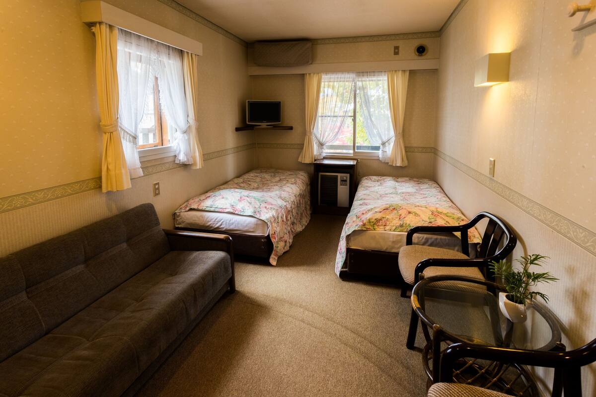 Une chambre de taille modeste, équipée de deux lits simples, d’un canapé, d’une petite table et d’un téléviseur.