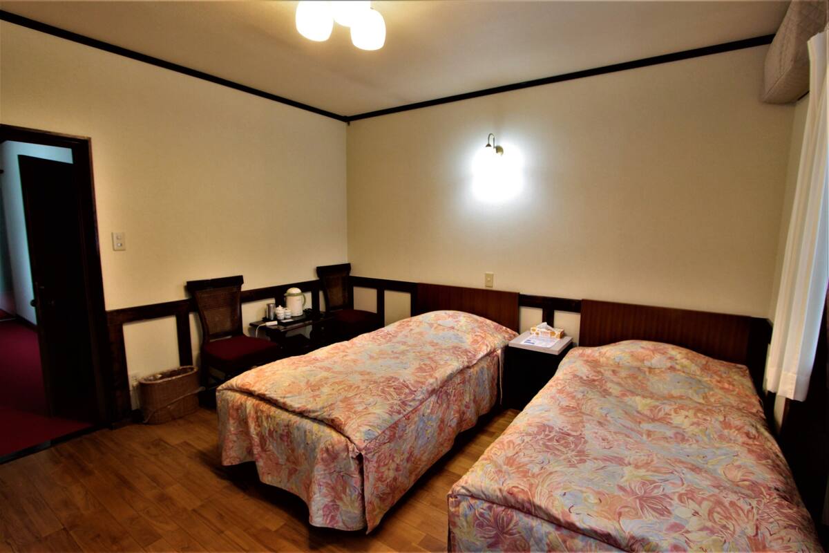 Une chambre avec deux lits, une chaise, une petite table et un luminaire fixé au mur.