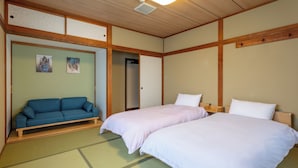 A traditional Japanese-style room with tatami flooring, a blue sofa, two beds with white bedding, and artwork on the walls. - Pension EastMountain Hakuba (Hakuba)