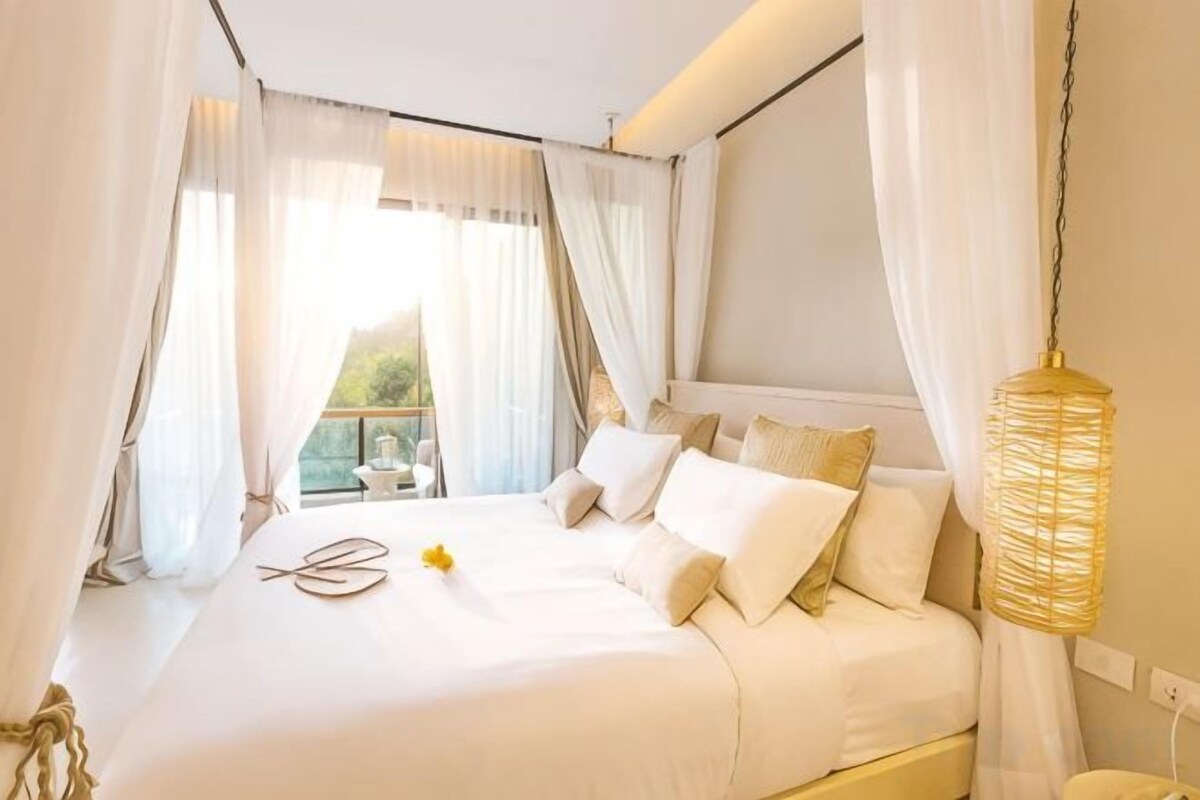 Un dormitorio con cama, cortinas, una lámpara colgante y una ventana.