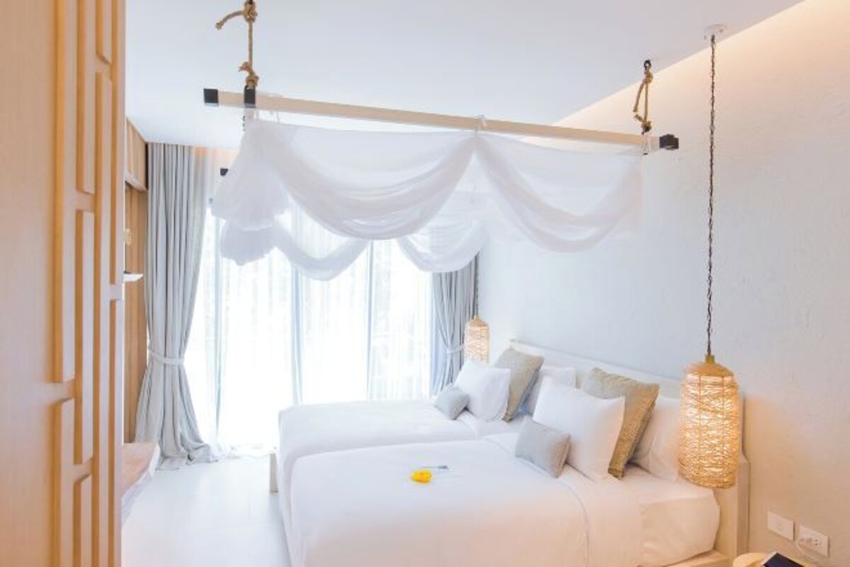 A hotel room with a large bed, a hanging light fixture, and a window with curtains.