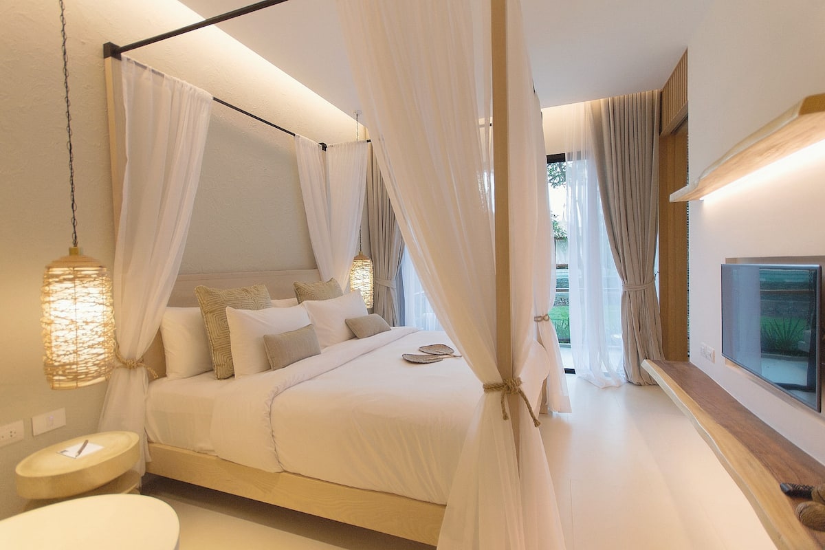 Un dormitorio con cama con dosel, una mesita de noche, un televisor y vistas al exterior.