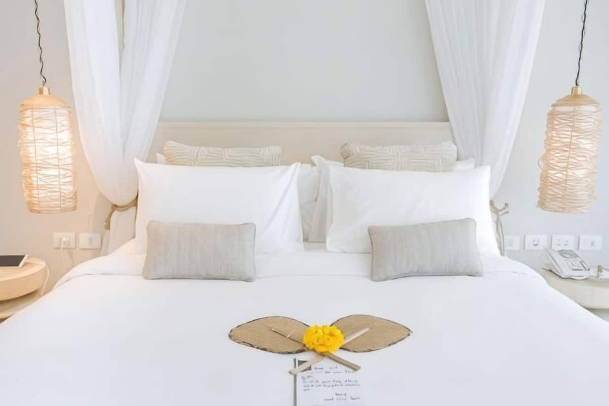 Una cama bien arreglada con ropa blanca, un abanico decorativo y una pequeña flor amarilla.