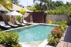 Piscina rectangular con un deck de madera alrededor, equipada con sillones de descanso y una sombrilla.