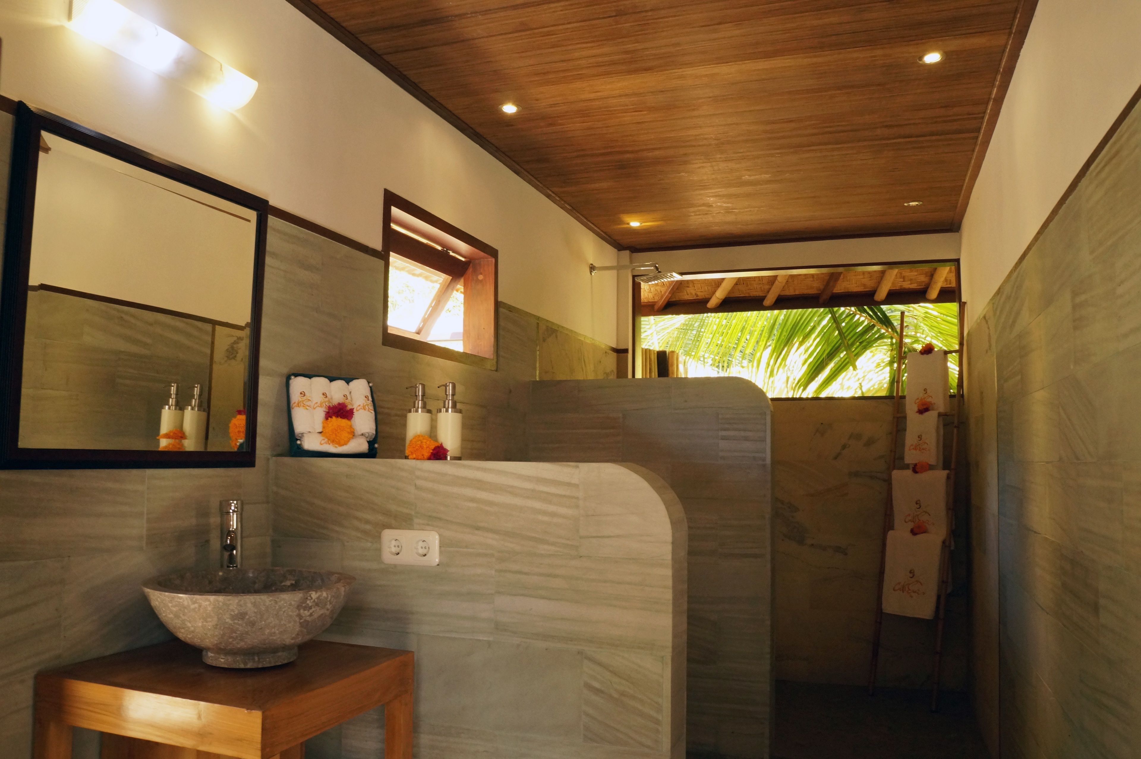 A bathroom with a stone sink, a mirror, and a shower area.