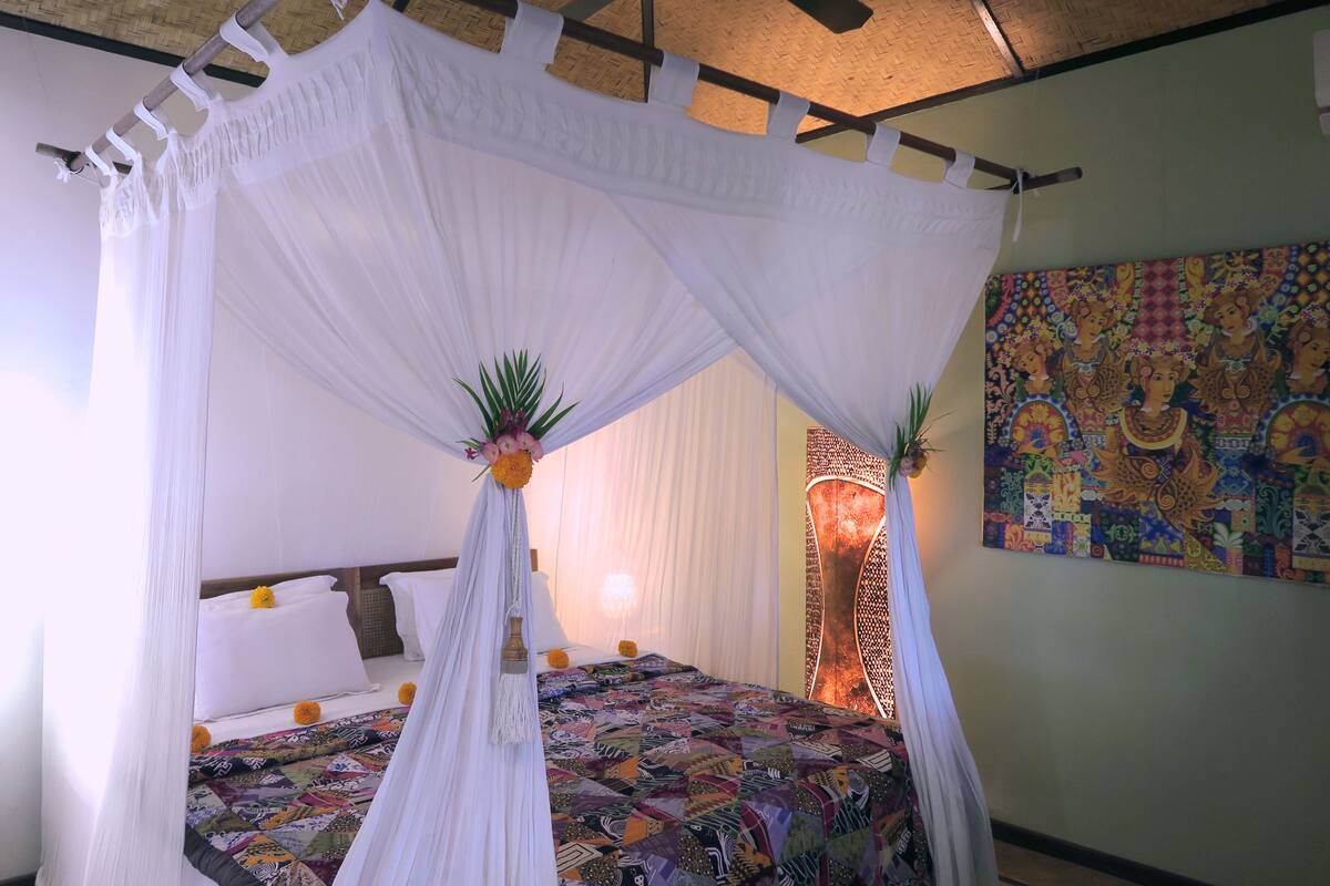 A room with a four-poster bed, a colorful quilt, and a decorative wall hanging.
