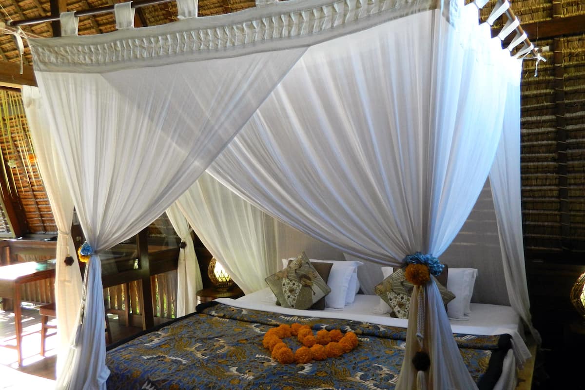 A four-poster canopy bed with a patterned bedspread and a cluster of orange flowers.