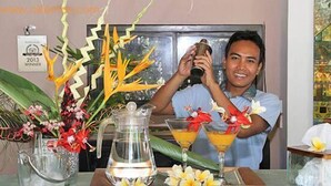 Un hombre preparando bebidas en una mesa, con una jofaina, vasos y flores decorativas.