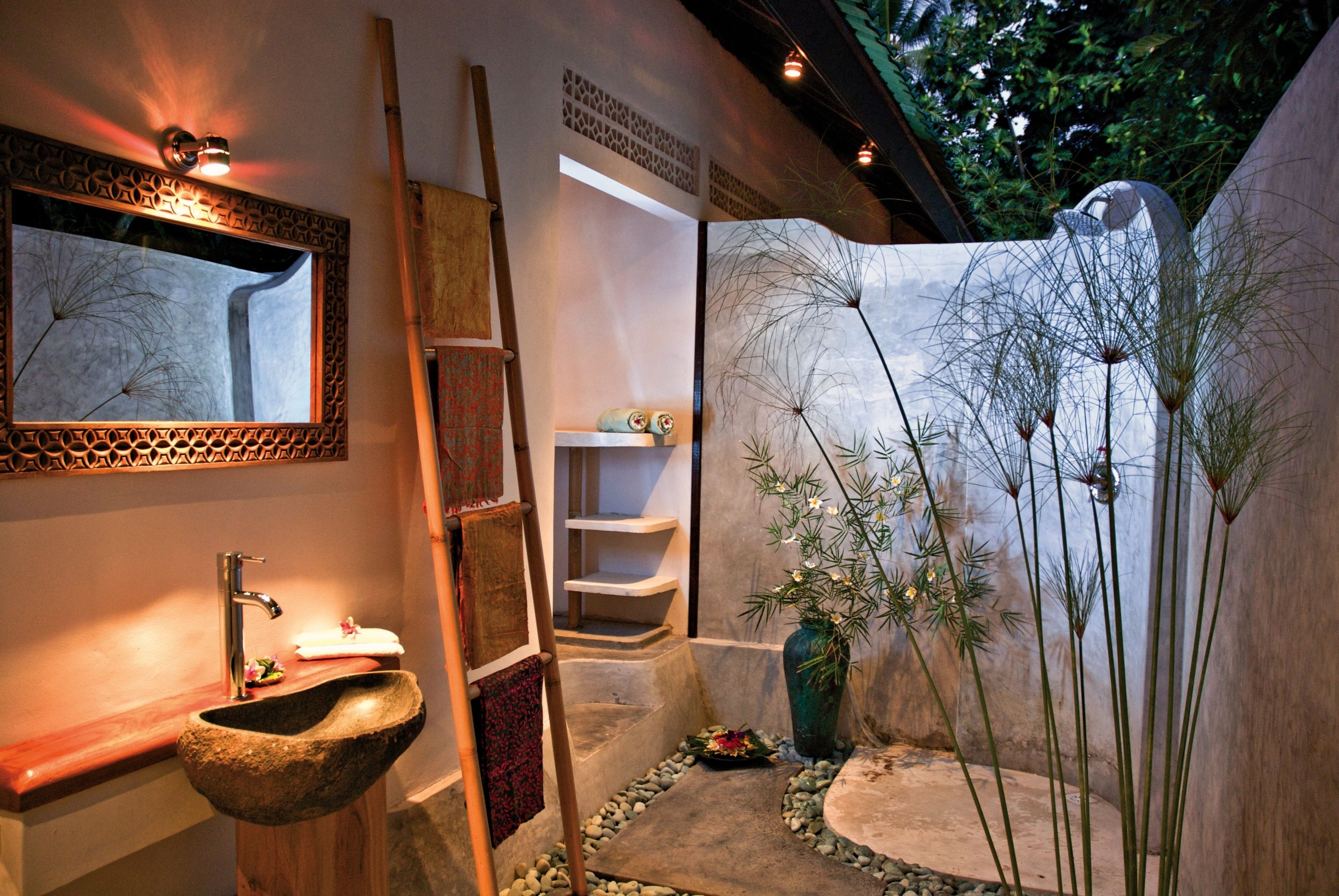 A bathroom with a stone sink, a mirror, a towel rack, a wooden ladder, a shelf with toiletries, and a decorative plant arrangement.
