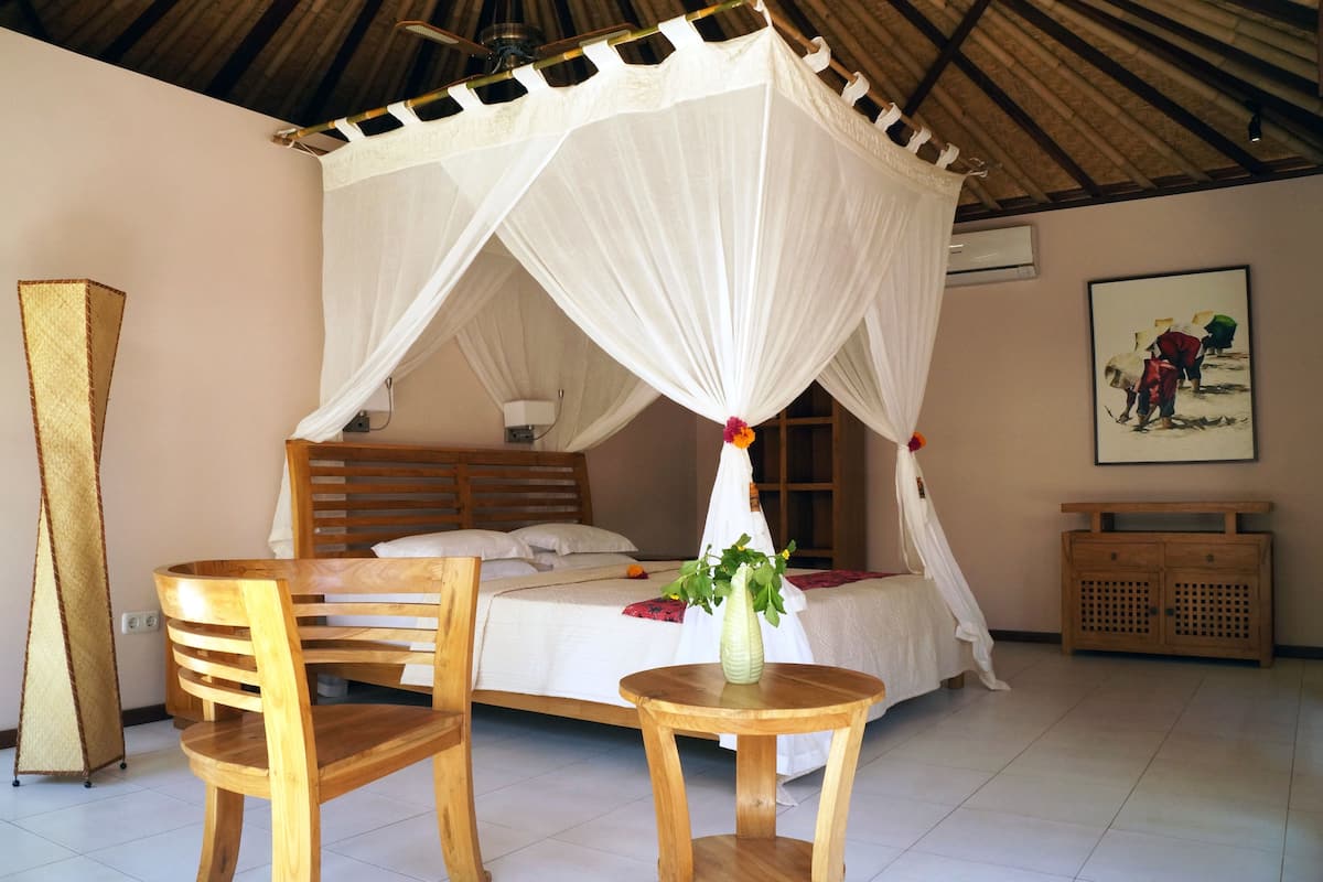 A room with a bed under a white canopy, wooden furniture, a small table with a vase, and a painting on the wall.