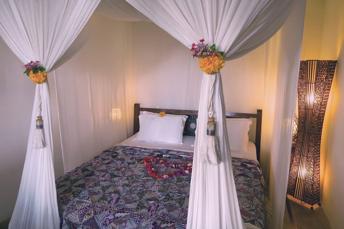 A bed with a patterned bedspread, white curtains, and a decorative flower arrangement on the headboard.