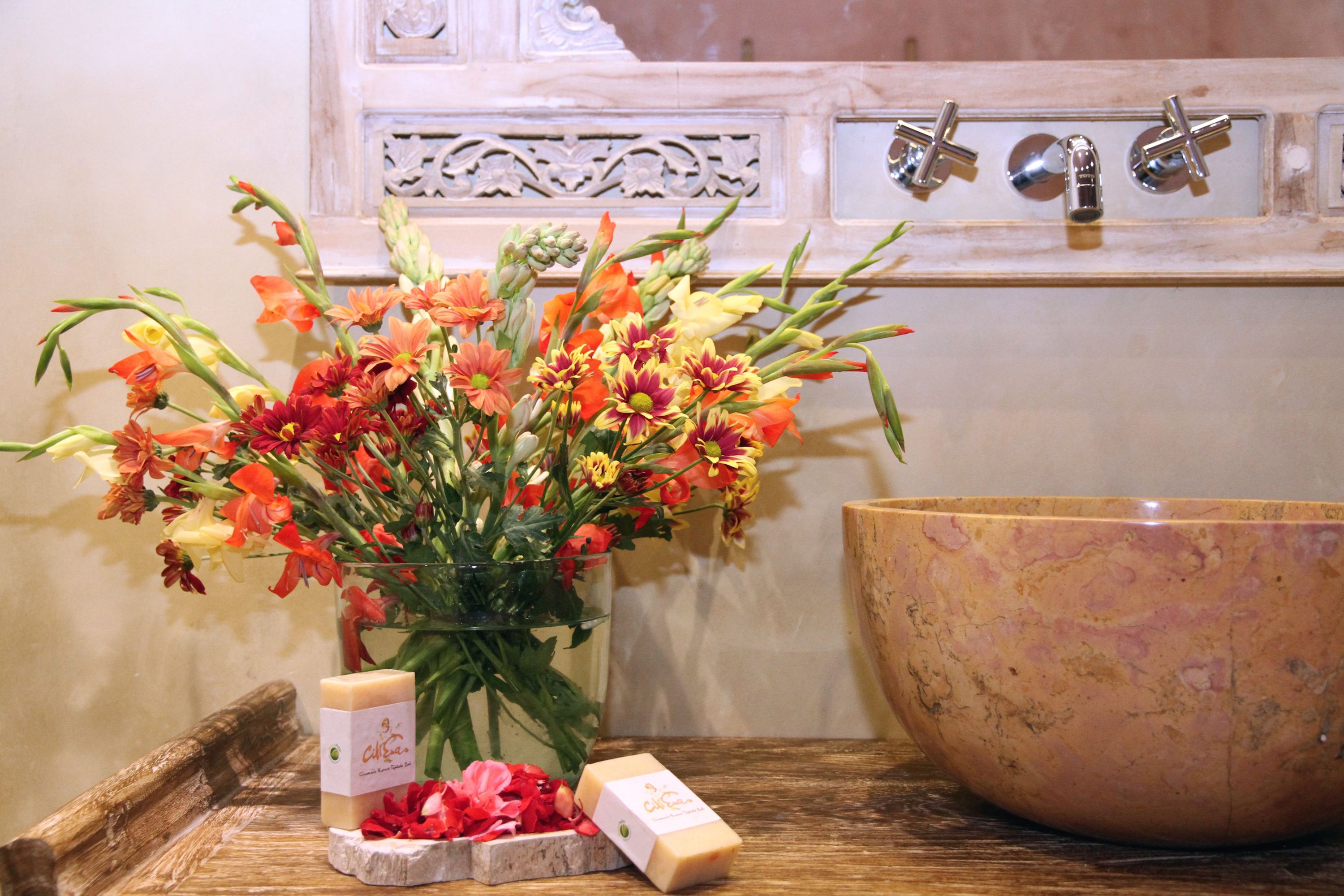 A wooden table with a large bowl, a vase of flowers, and a bar of soap.