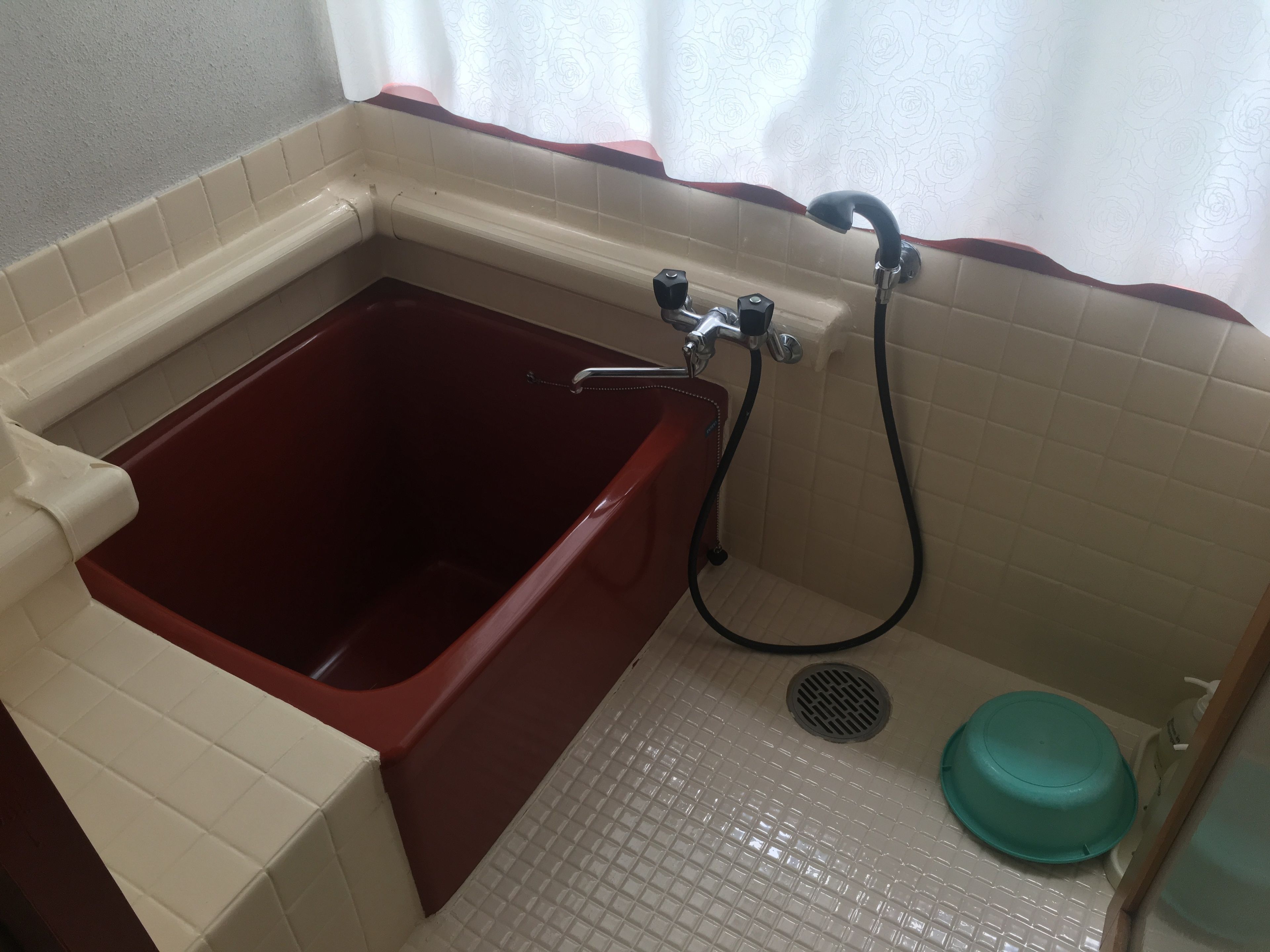 A bathroom with a red bathtub, a showerhead, and a green basin.