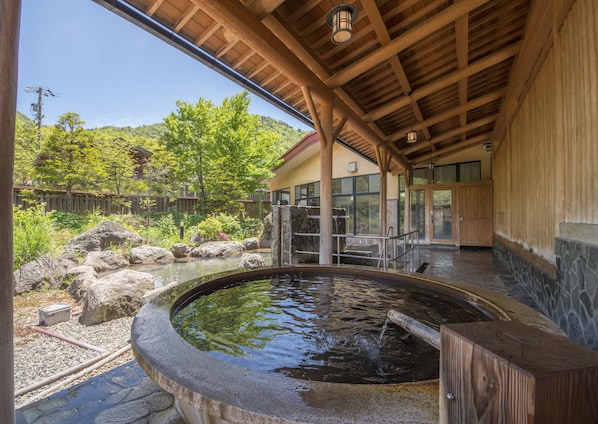 A traditional Japanese onsen with a stone bath, wooden beams, and a view of a forested hillside. - Nakamurakan (Takayama)