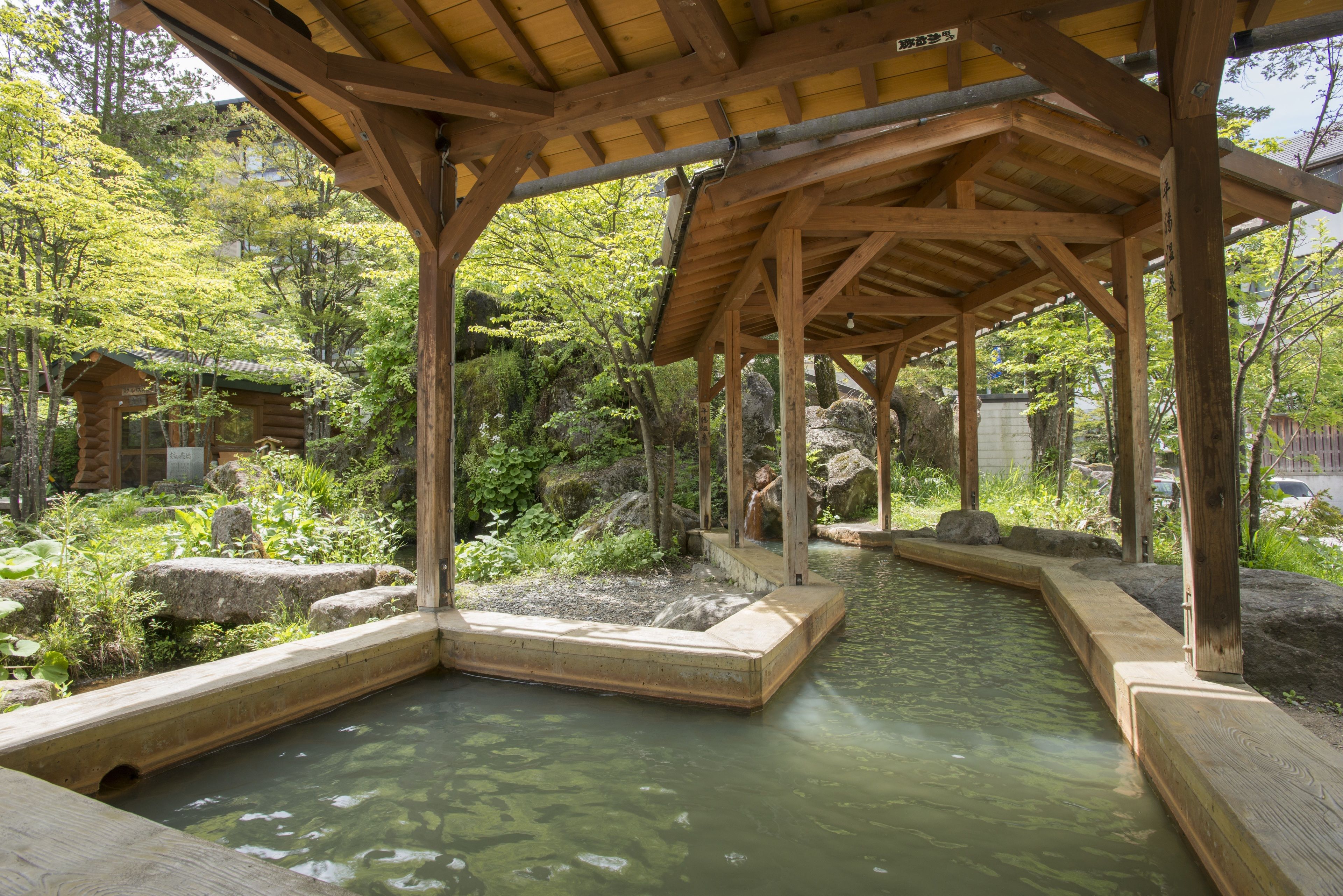 A wooden pavilion with a stone pathway leading to a water feature surrounded by greenery.