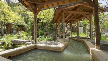A wooden pavilion with a stone pathway leading to a water feature surrounded by greenery.