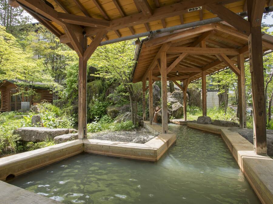 A wooden pavilion with a stone pathway leading to a water feature surrounded by greenery.