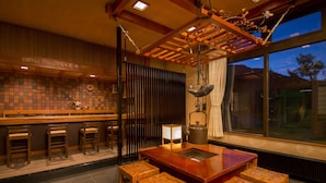 A cozy bar area with wooden stools, a central table, and a hanging light fixture. - Nakamurakan (Takayama)