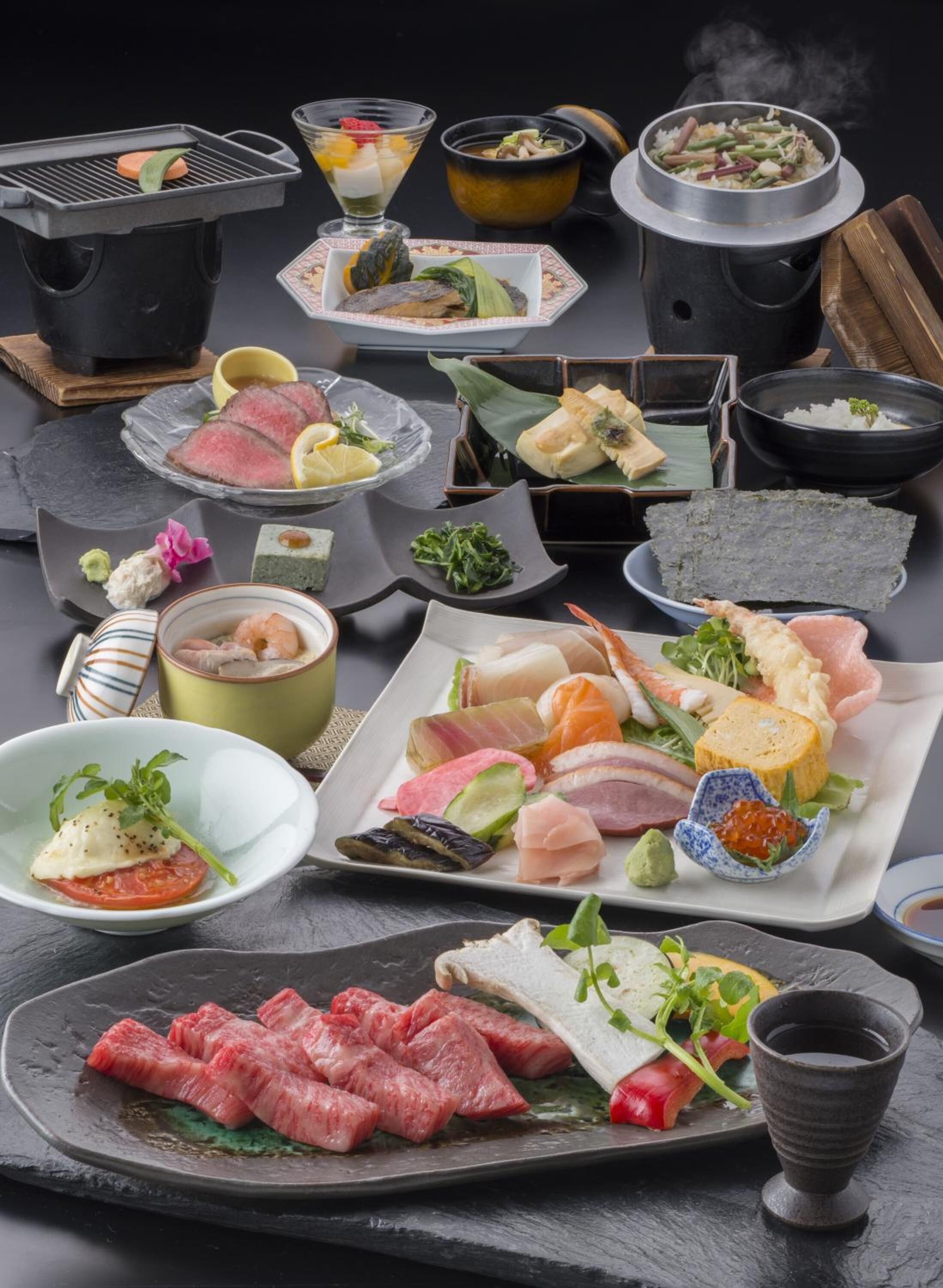 Variedad de platos japoneses, incluyendo sushi, sashimi y carnes a la parrilla, presentados sobre una mesa de pizarra con fondo negro.