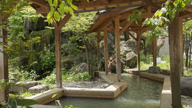 A wooden pavilion with a stone platform over a small pond, surrounded by lush greenery and rocks. - Nakamurakan (Takayama)