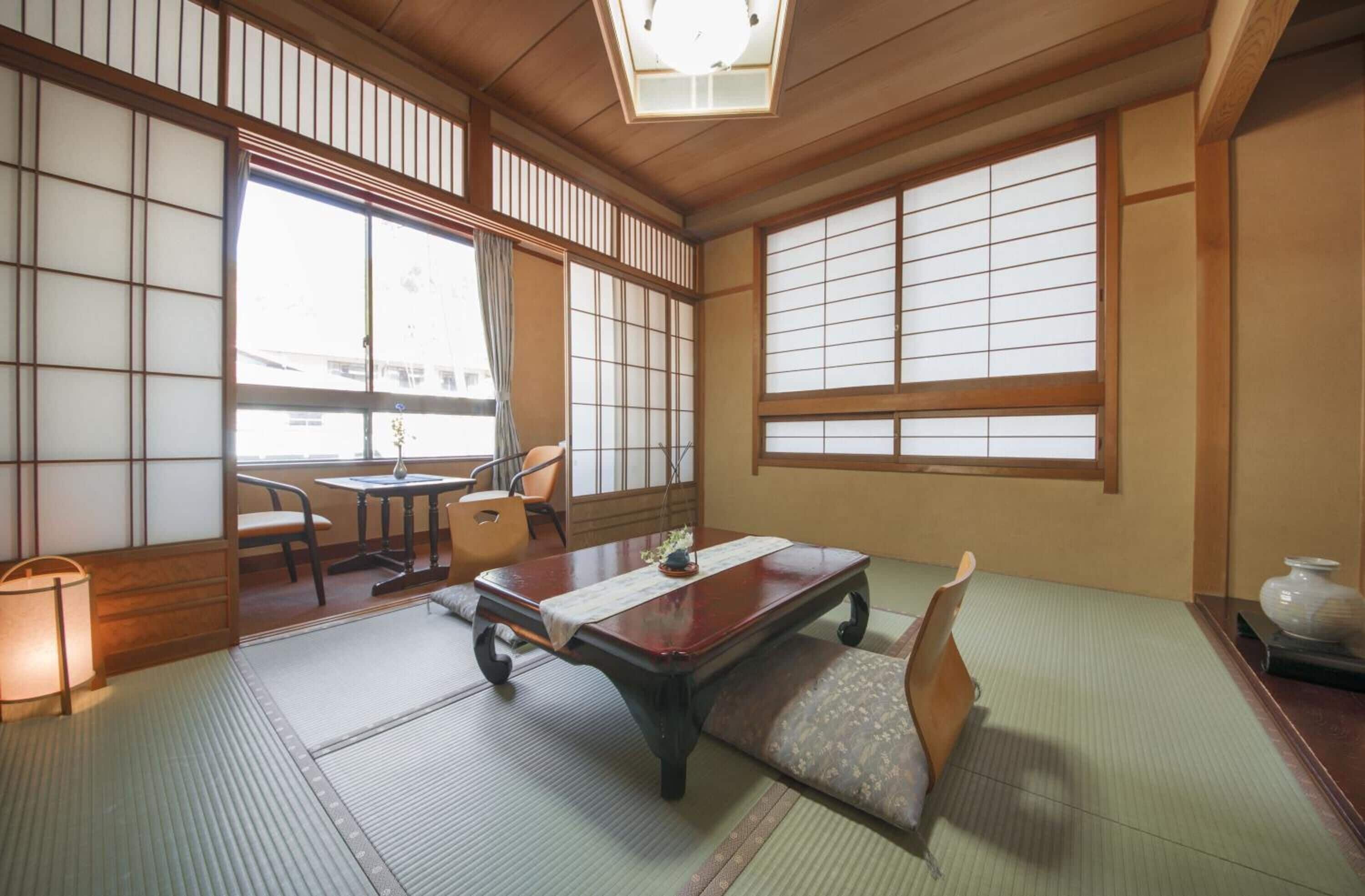 A traditional Japanese room with tatami flooring, a low table, a cushioned bench, and sliding shoji doors.