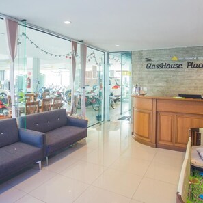 A reception area with a counter, seating, and a view of parked vehicles through glass doors. - The Glasshouse Place (Trang)