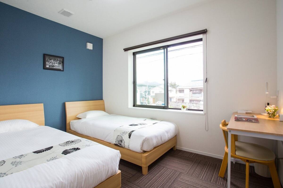 Une chambre avec deux lits, un bureau et une fenêtre donnant sur des immeubles.