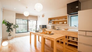 A modern kitchen with wooden flooring, a dining table, and a built-in oven. - Mulan Hostel (Kyoto)